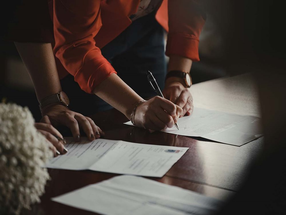 A person signing paperwork at a desk.